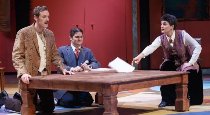 Gertrude Stein (Laurel Semerdjian) offers ‘feedback’ on a surprised Ernest Hemingway’s (Matthew Scollin) manuscript while an amused F. Scott Fitzgerald (Adam Bonanni) watches. Photo via David Bachman Photography.