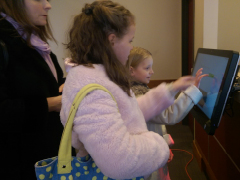 A woman stands behind two young girls checking in at a kiosk