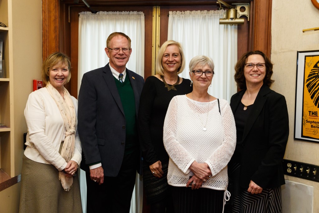 One well-dressed man and four well-dressed women pose for a picture 