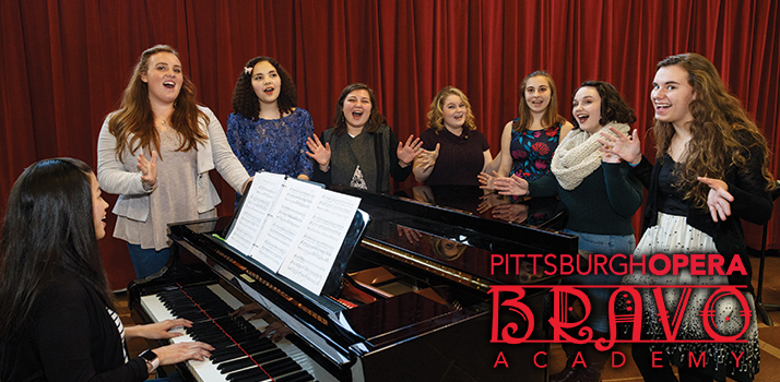 Photo of high school students singing by a piano at the Bitz Opera Factory